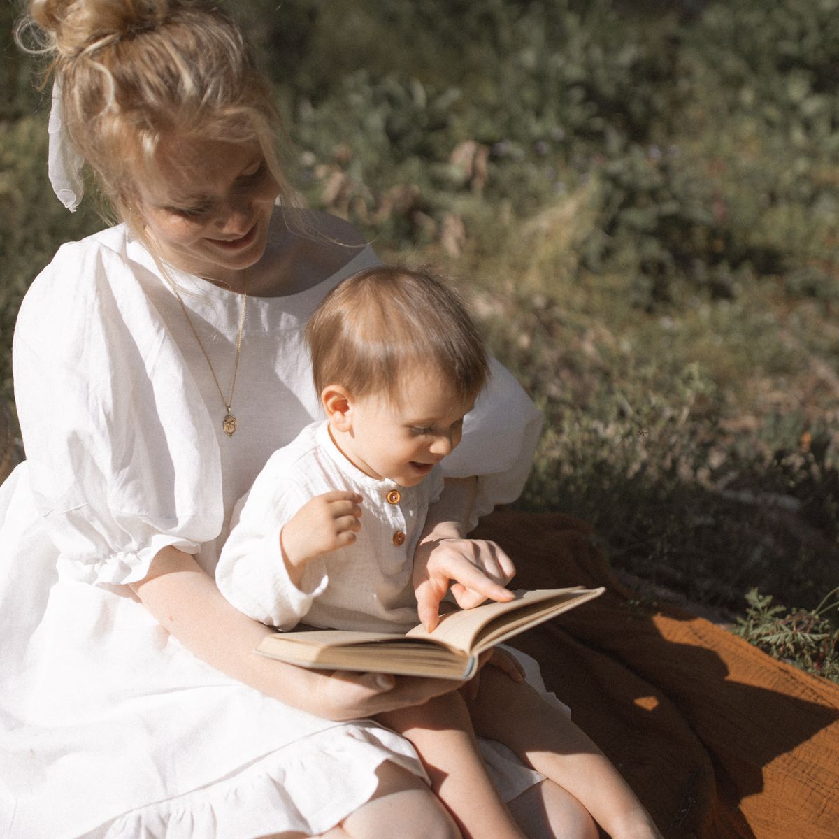 A parent and child reading a book together outdoors