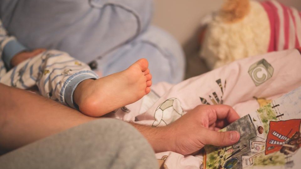 A baby resting on a parent’s lap while an illustrated picture book is held open at bedtime